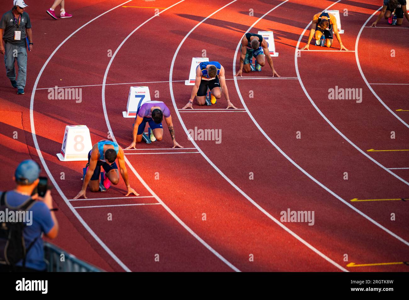 B. BYSTRICA, SLOVACCHIA, 20 LUGLIO 2023: Maschi Sprinters in posa all'inizio della 200m Race Under Serene Sunset Light Foto Stock