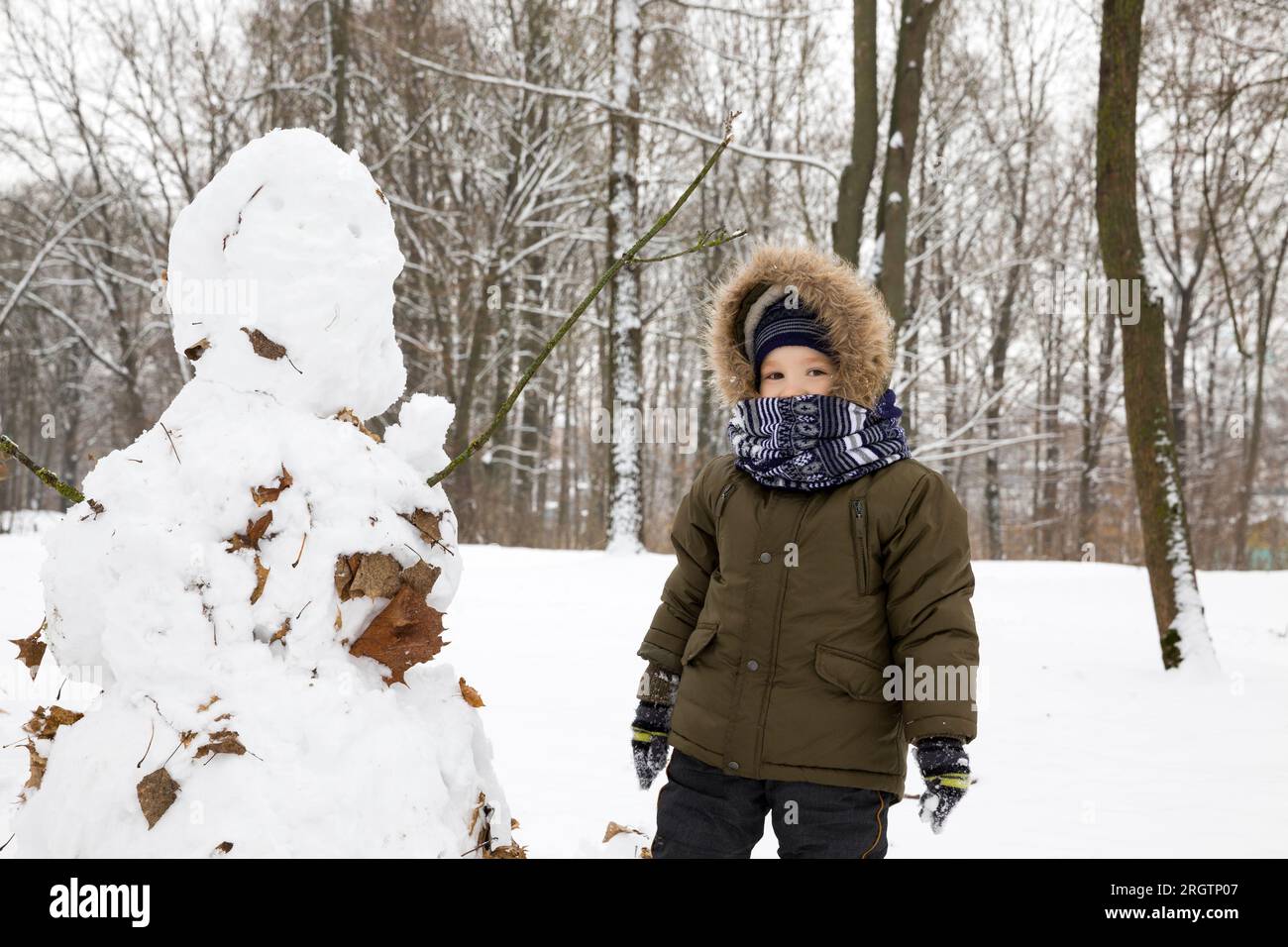 Il ragazzo ha messo il suo pupazzo di neve a Winter Park, dal pupazzo di neve che esce da un gran numero di foglie cadute, resta nel parco all'aperto Foto Stock