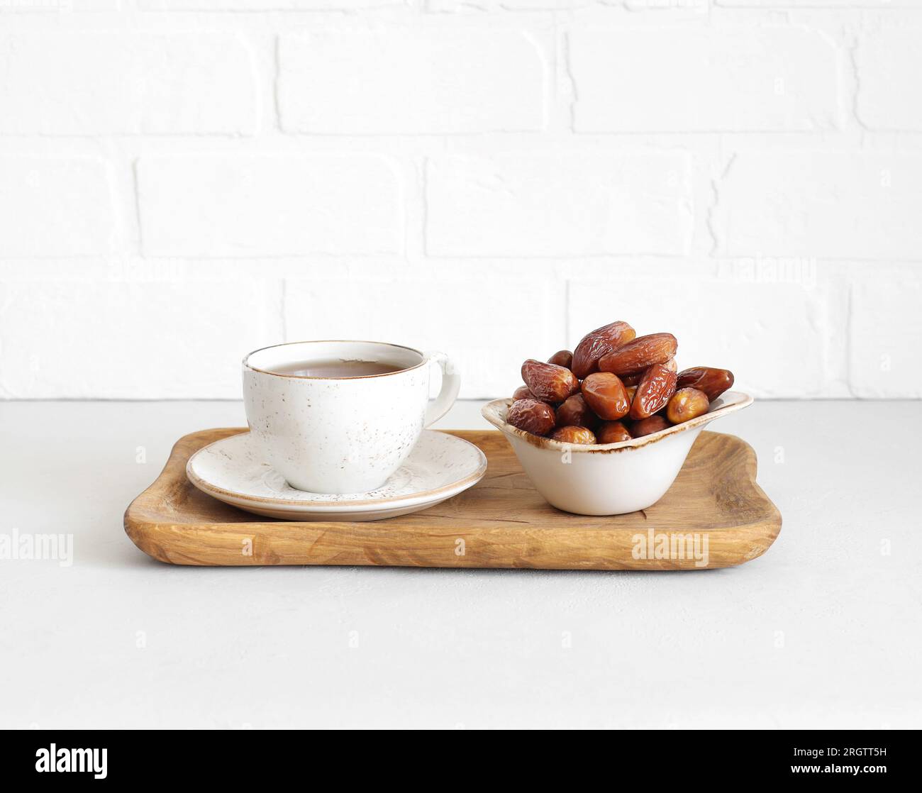 Datteri essiccati in una ciotola e una bevanda da tè in un vassoio di legno su sfondo bianco. Cibo popolare per il Ramadan. Dolci orientali. Foto Stock