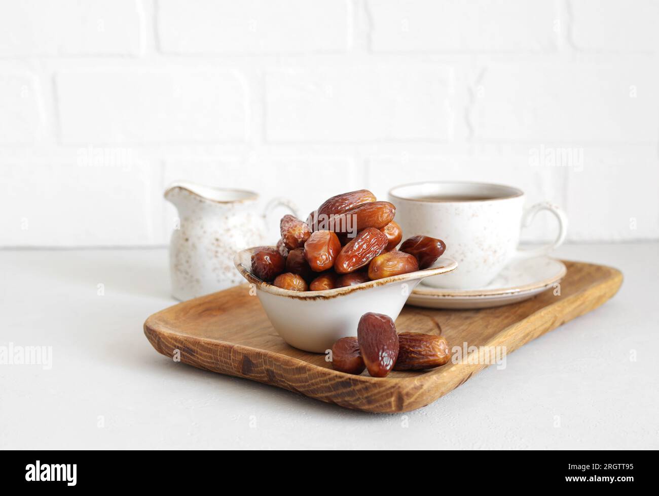 Primi piani di date essiccate in una ciotola su sfondo bianco. Datteri, tè e caraffa del latte in un vassoio di legno Cucina tradizionale araba. Foto Stock