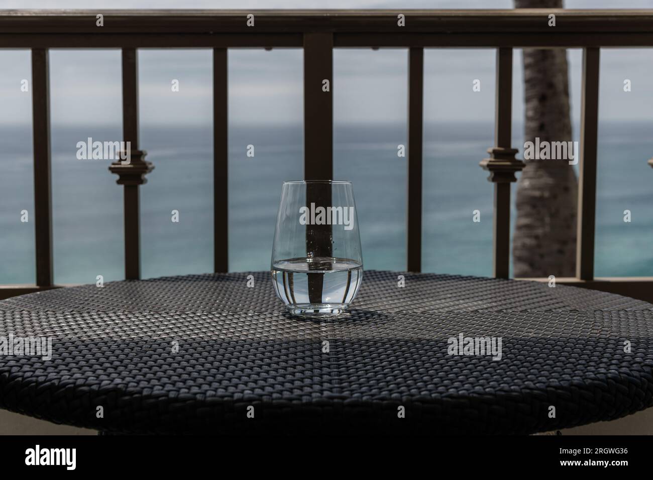 Mezzo bicchiere d'acqua su un tavolo rotondo in un balcone che si affaccia sull'oceano Pacifico in un resort della California meridionale Foto Stock