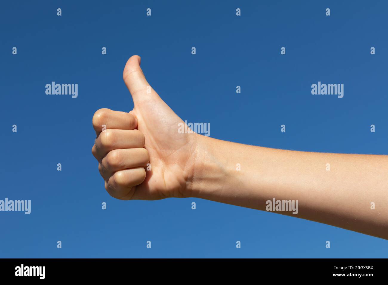 Il bambino mostra un gesto con i pollici verso l'alto contro il cielo blu, un concetto sul tema del clima limpido e soleggiato Foto Stock