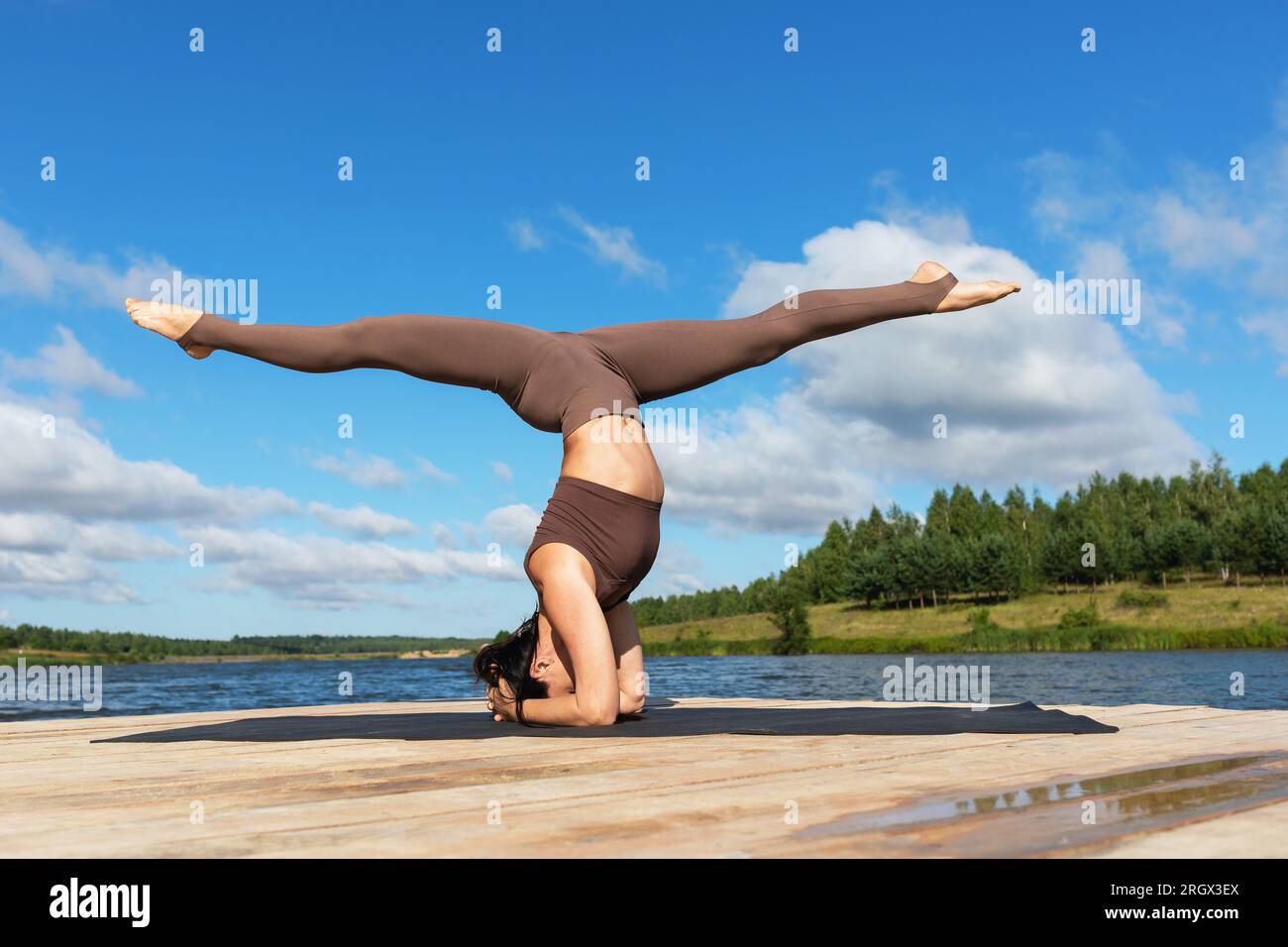 Una donna che pratica yoga esegue l'esercizio Sirshasana con Hanumanasana, un asana invertito con uno spago longitudinale, si allena in abbigliamento sportivo sulla S Foto Stock