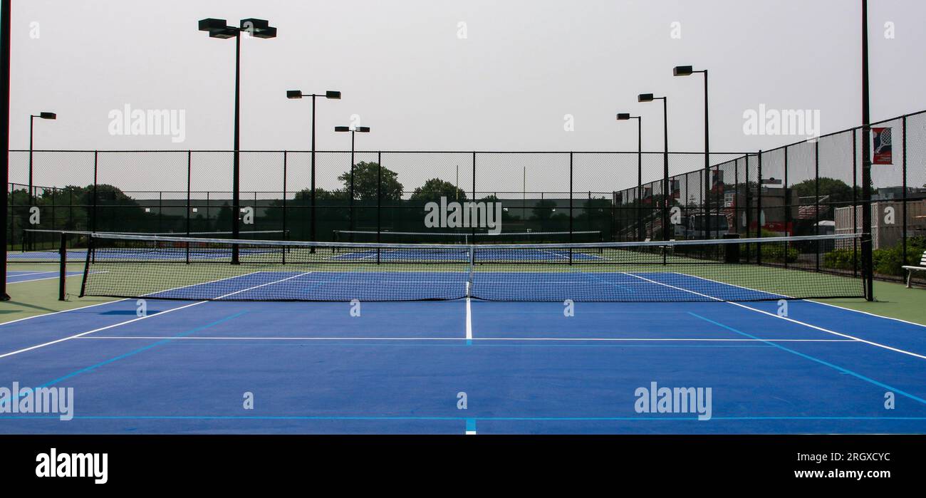 Vista frontale dei campi da tennis blu e verdi con luci circondate da alte scherma nere. Foto Stock