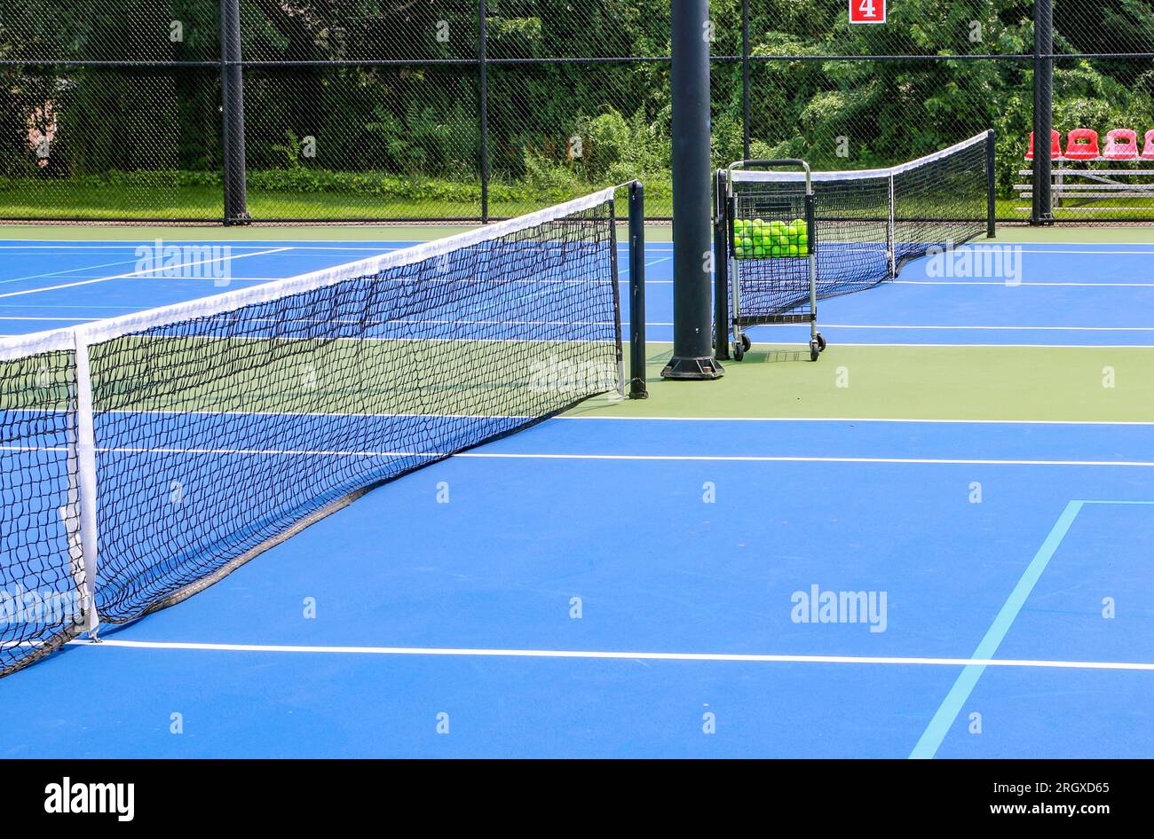 Vista laterale di un campo da tennis blu e verde con un cart pieno di palle da tennis racchiuse con scherma nera. Foto Stock