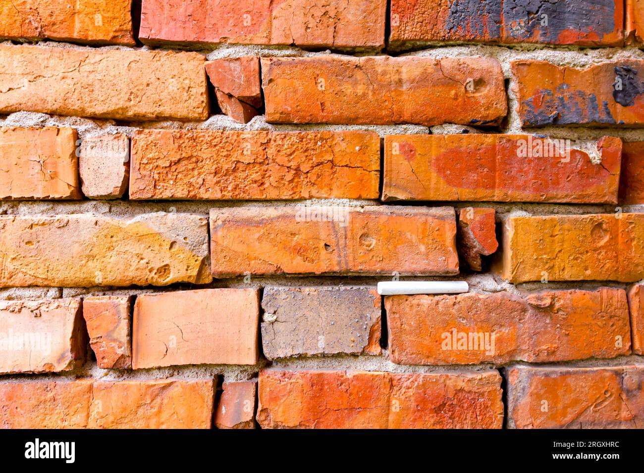 Il gesso della scuola bianca è bloccato in un muro obsoleto e fatiscente di mattoni rossi danneggiati. Foto Stock