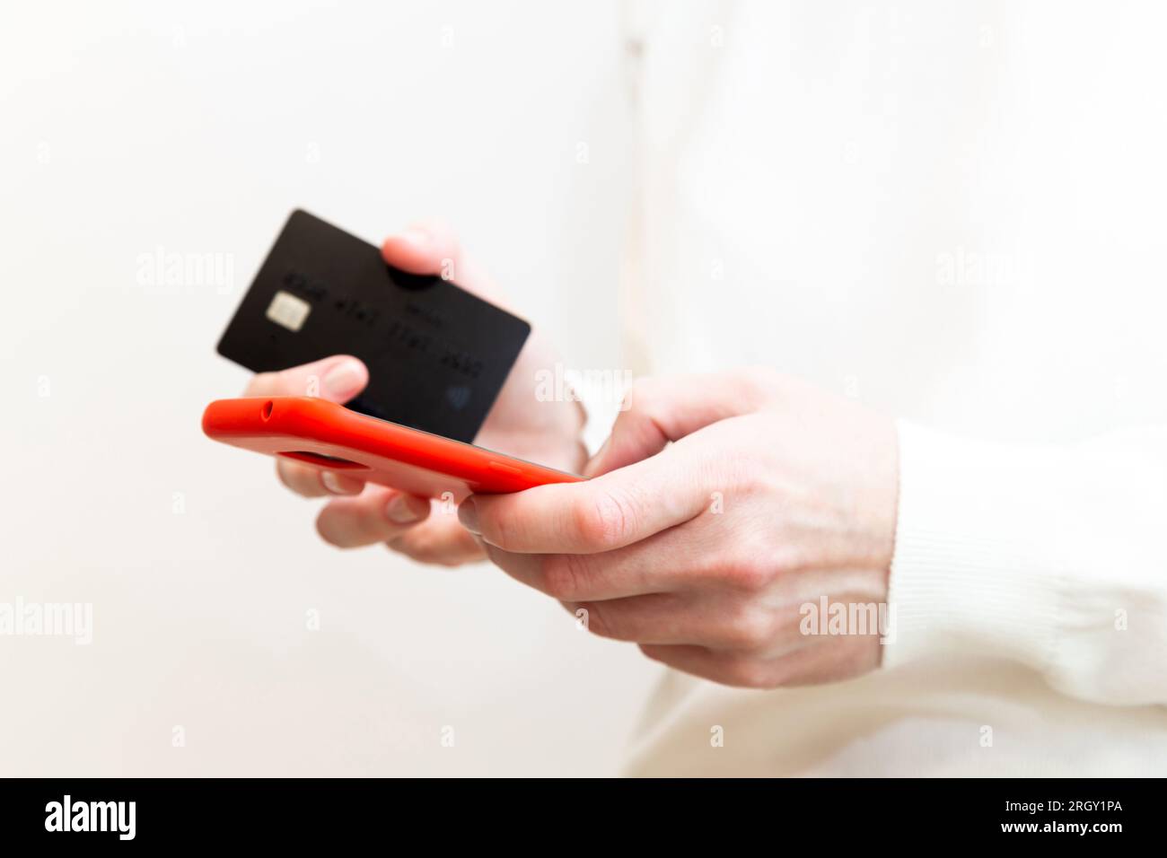 Primo piano delle mani femminili che tengono la carta di credito e utilizzano lo smartphone in custodia rossa su sfondo bianco. Donna che paga in modo sicuro online, utilizzando il servizio bancario Foto Stock