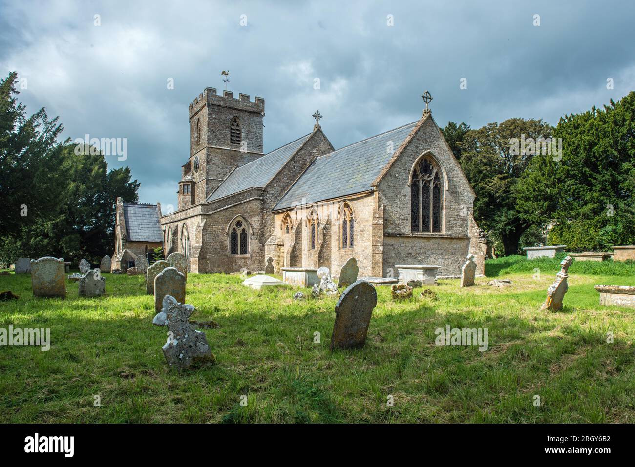 Chiesa di Santa Maria Vergine Powerstock nella contea di Dorset in un luminoso giorno di settembre con alcune nuvole che abbelliscono il cielo e con un cimitero. Foto Stock