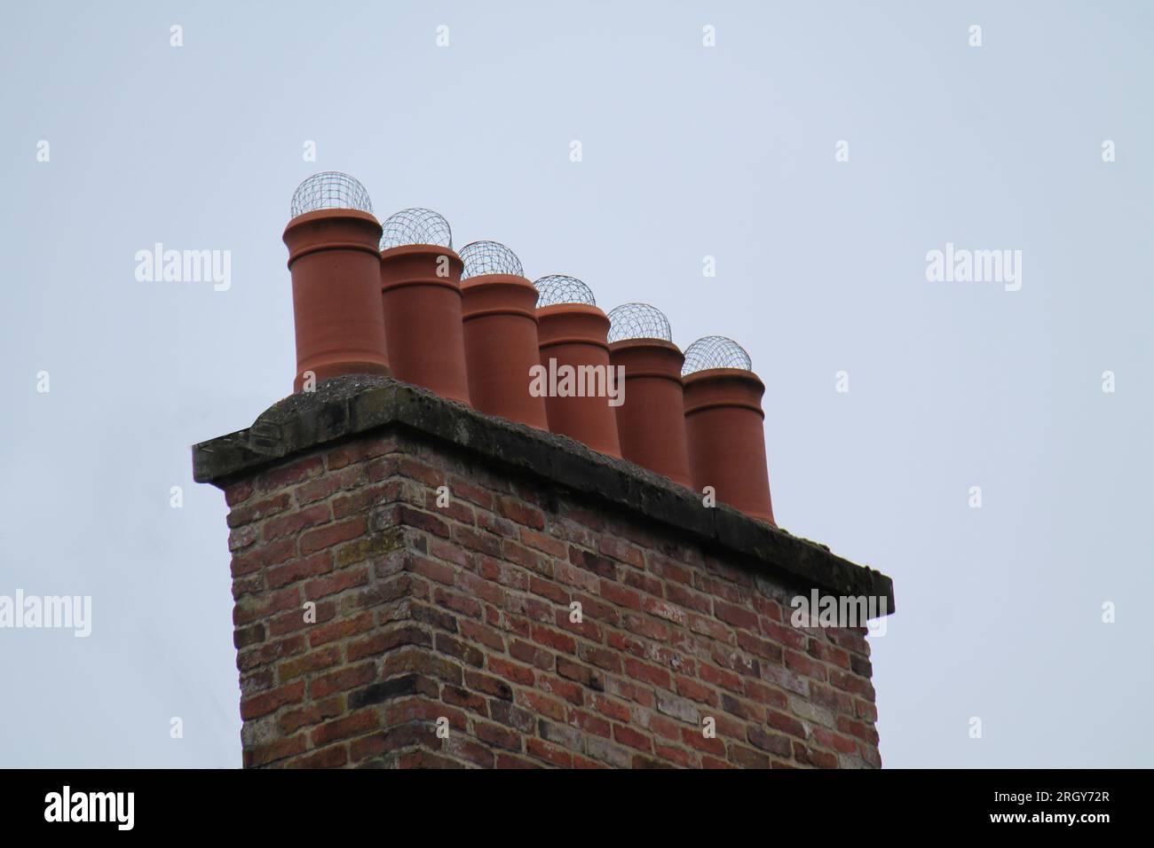 Una fila di sei pentole di camino in terracotta con copertura in rete. Foto Stock