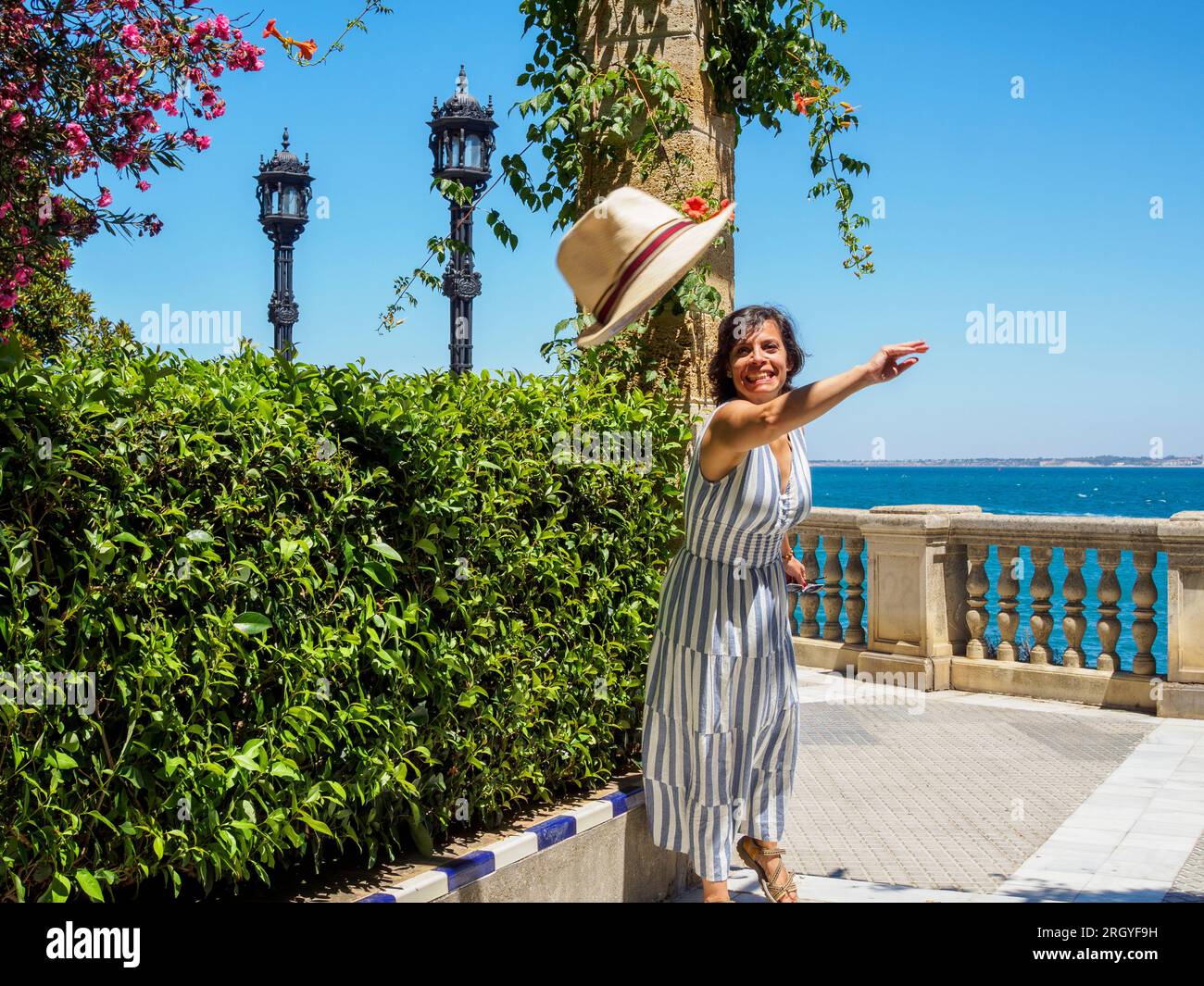 Una turista caucasica che lancia il suo cappello di paglia alla macchina fotografica. Clara Campoamor Gardens. Cadice, Andalusia, Spagna. Foto Stock