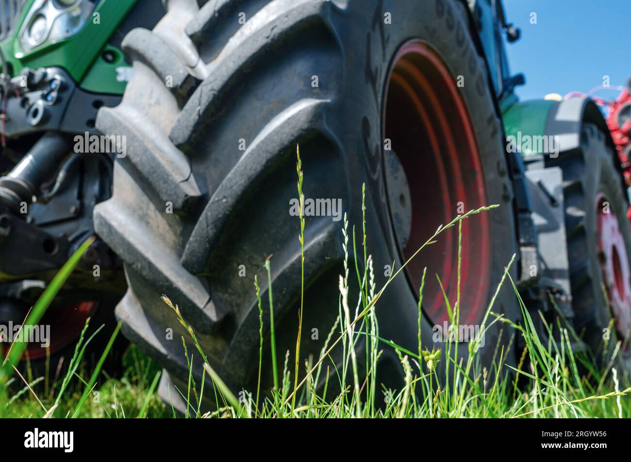 Vista angolare bassa attraverso l'erba alla ruota del trattore. Paesaggio agricolo Foto Stock