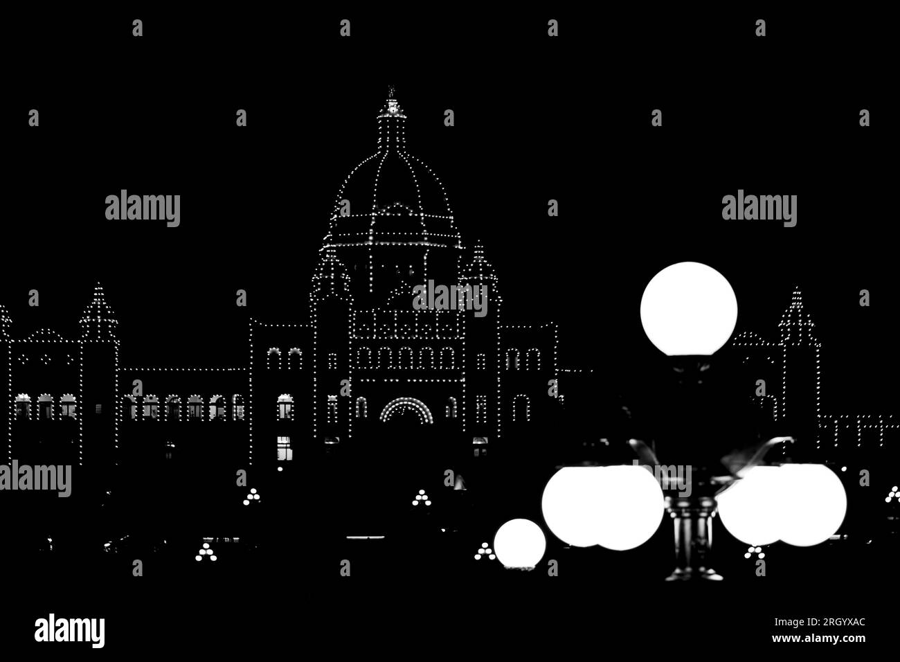 Silhouette illuminata del Parlamento della Columbia Britannica. Luci stradali illuminate in primo piano. Fotografia in bianco e nero. Victoria, Canada. Foto Stock