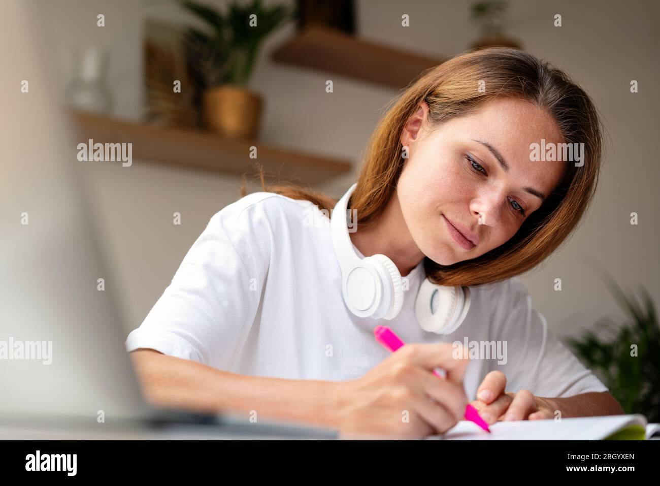 Una giovane studentessa universitaria moderna fa i compiti sedendo alla scrivania a casa. Foto Stock