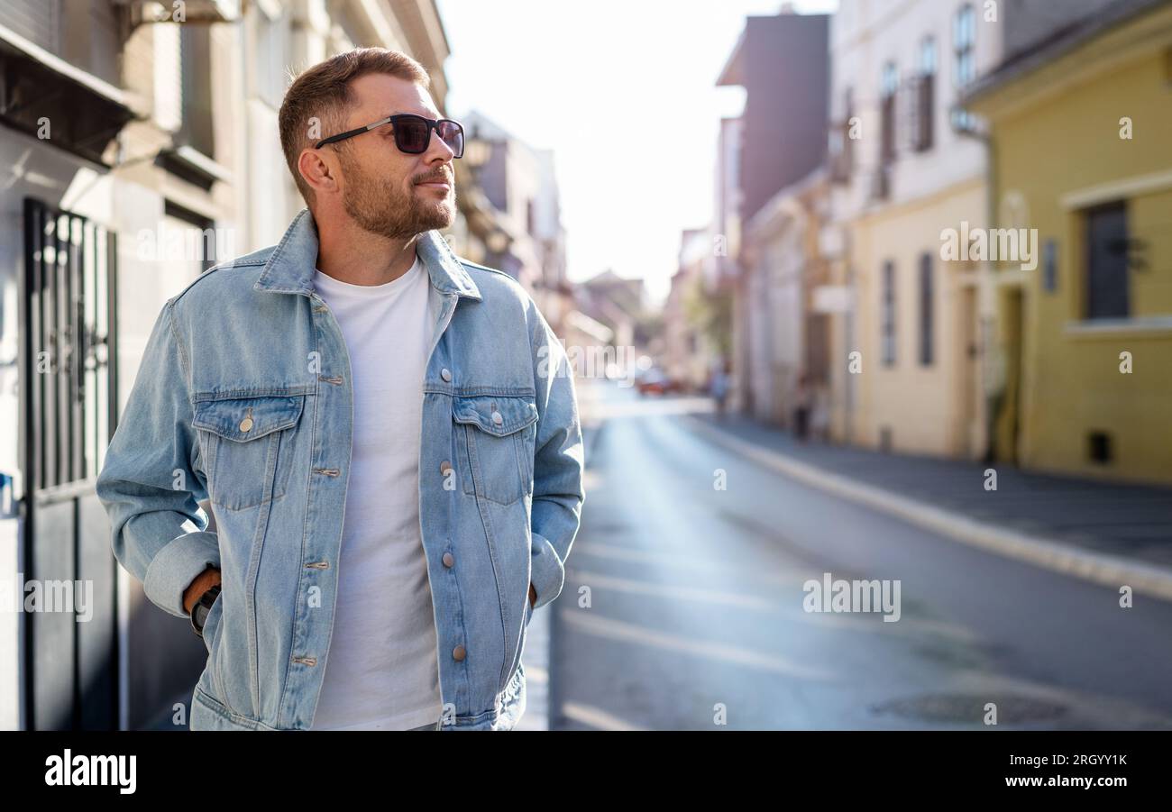 Una bella bruna giovane adulto con occhiali da sole e una giacca in denim cammina per la città. Foto Stock