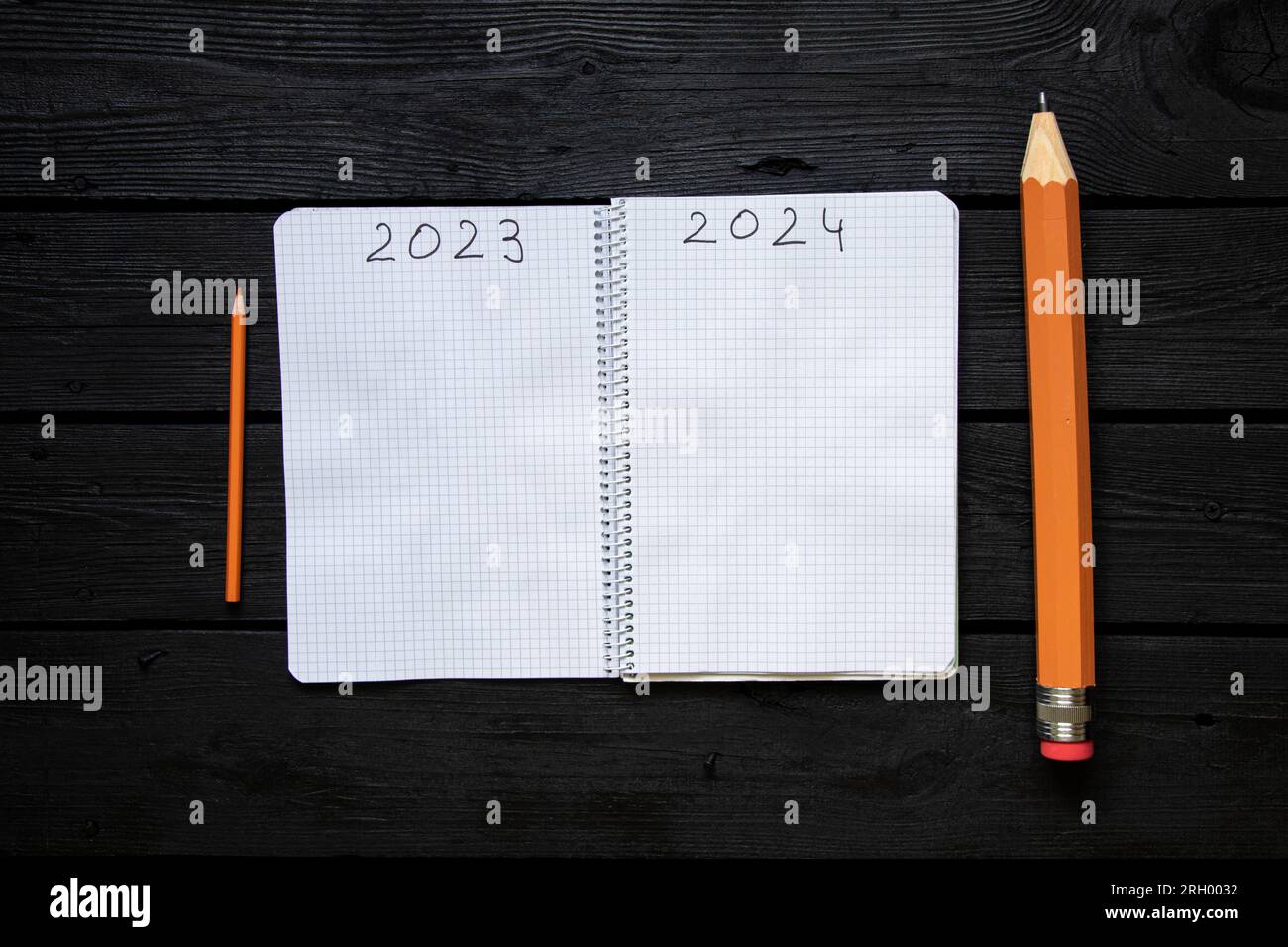 L'anno 2023 e 2024 è scritto sulle pagine di un quaderno e accanto ad esso si trova una matita grande e piccola su un tavolo nero, la fine del vecchio anno e' Foto Stock