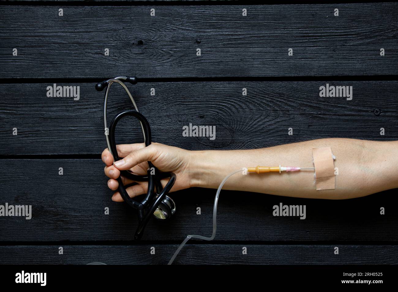 Un contagocce nelle mani di una ragazza e tiene in mano uno stetoscopio, che giace su uno sfondo di legno nero, medicine e cure, fanno una goccia Foto Stock