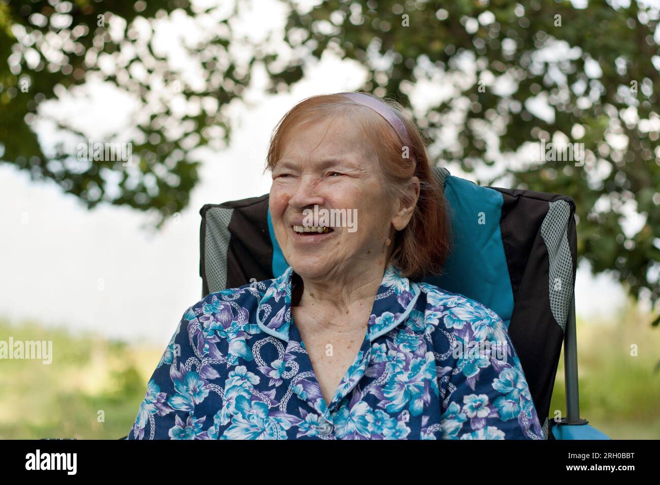 Ritratto della nonna anziana sorridente in giardino a casa. anziana con oltre 80 ridere, gioire, rilassarsi, sedersi in sedia, nella natura. Estate. Vecchio Foto Stock
