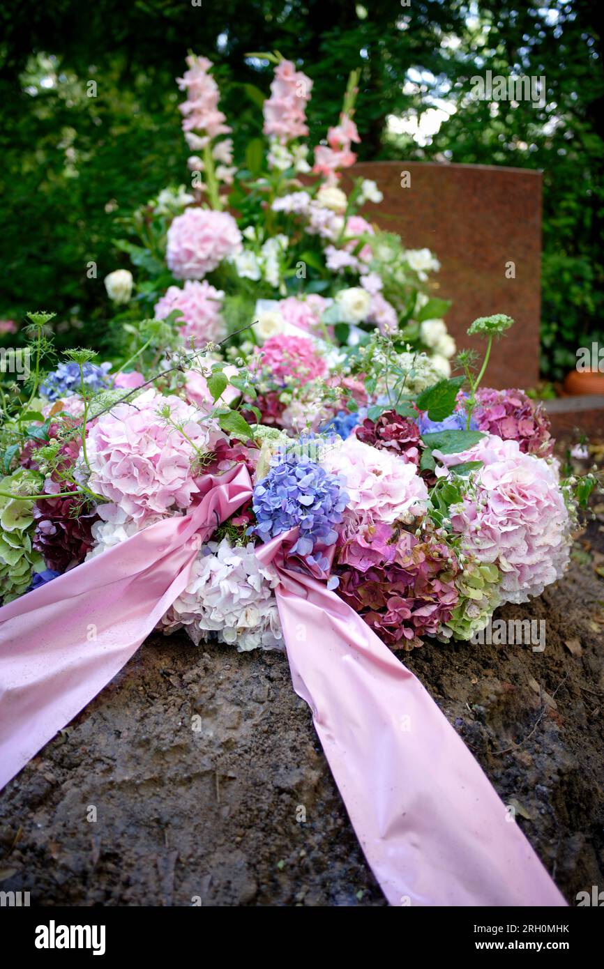 una corona di ortensie rosa, bianca e blu con un arco rosa in lutto su una tomba dopo un funerale Foto Stock