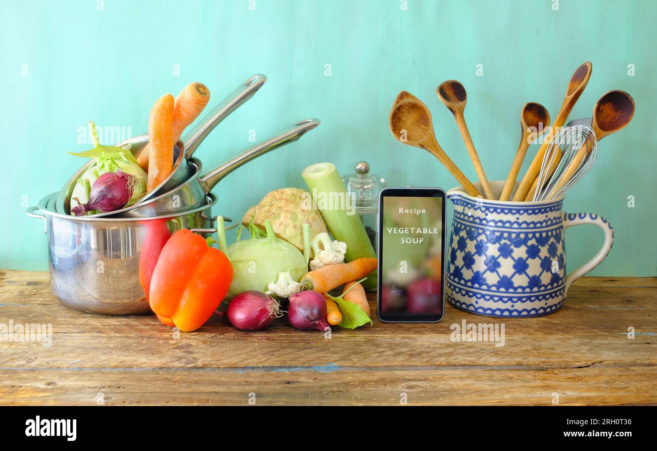 Vari utensili da cucina e verdure, smartphone che mostra la ricetta dei social media per la zuppa di verdure, spazio copia gratuito Foto Stock
