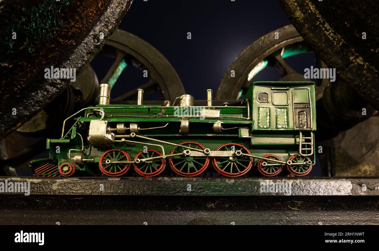Modello di locomotiva a vapore verde con ruote rosse sotto una serie di vecchie ruote per locomotive a vapore. Foto Stock