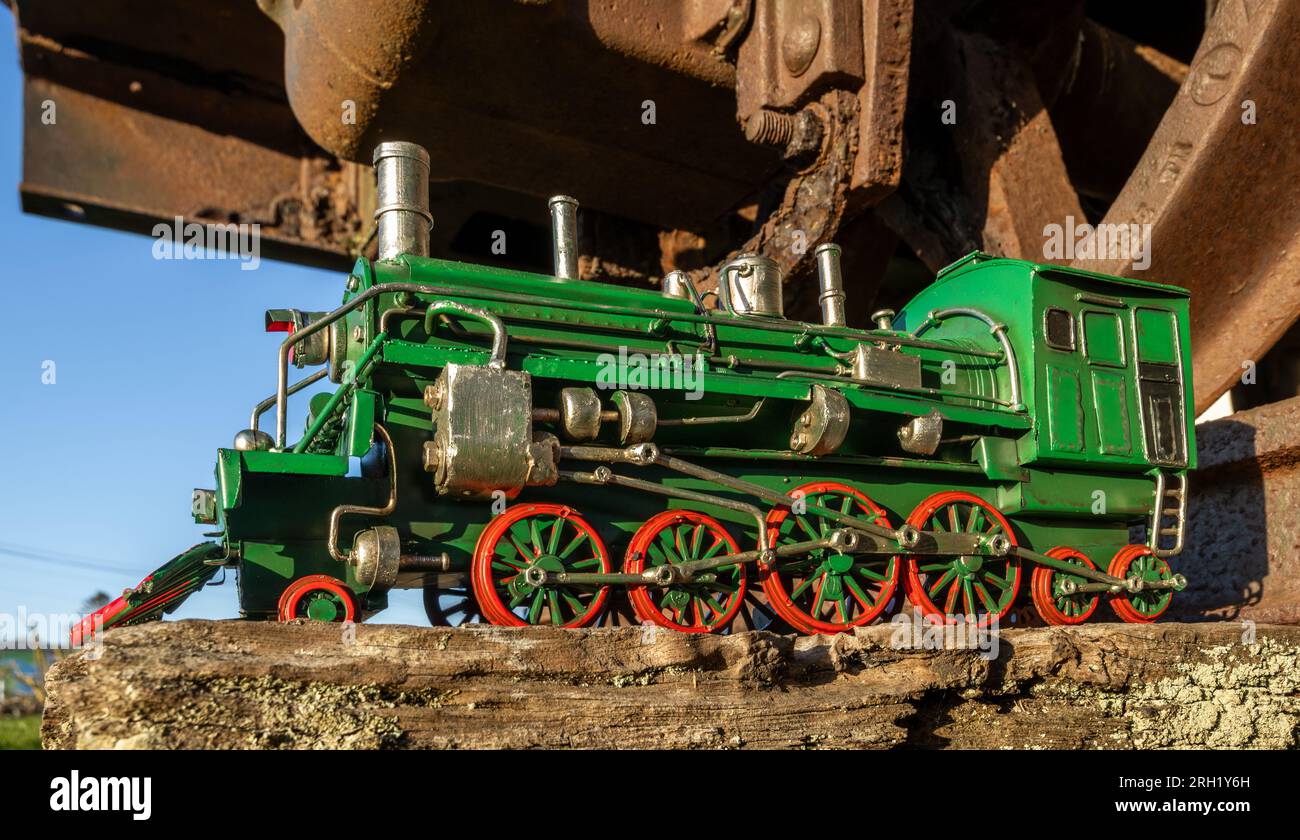 Modello di locomotiva a vapore verde con ruote rosse sotto un carro ferroviario. Foto Stock