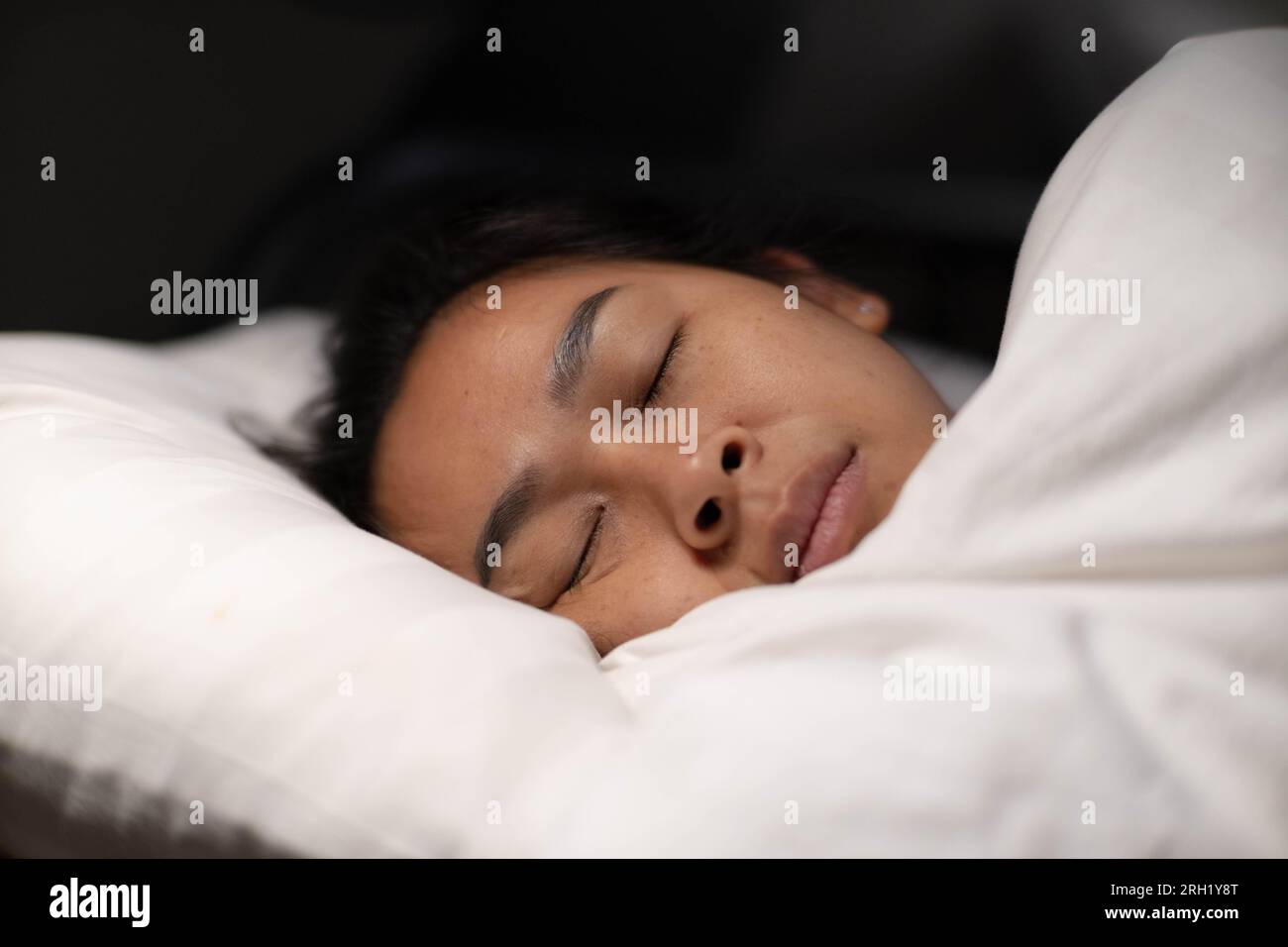 Donna asiatica che riposa coperta di coperta su lenzuola bianche in camera da letto. Donna che dorme. Donna tranquilla sdraiata a letto e tenendo gli occhi chiusi mentre è coperta Foto Stock