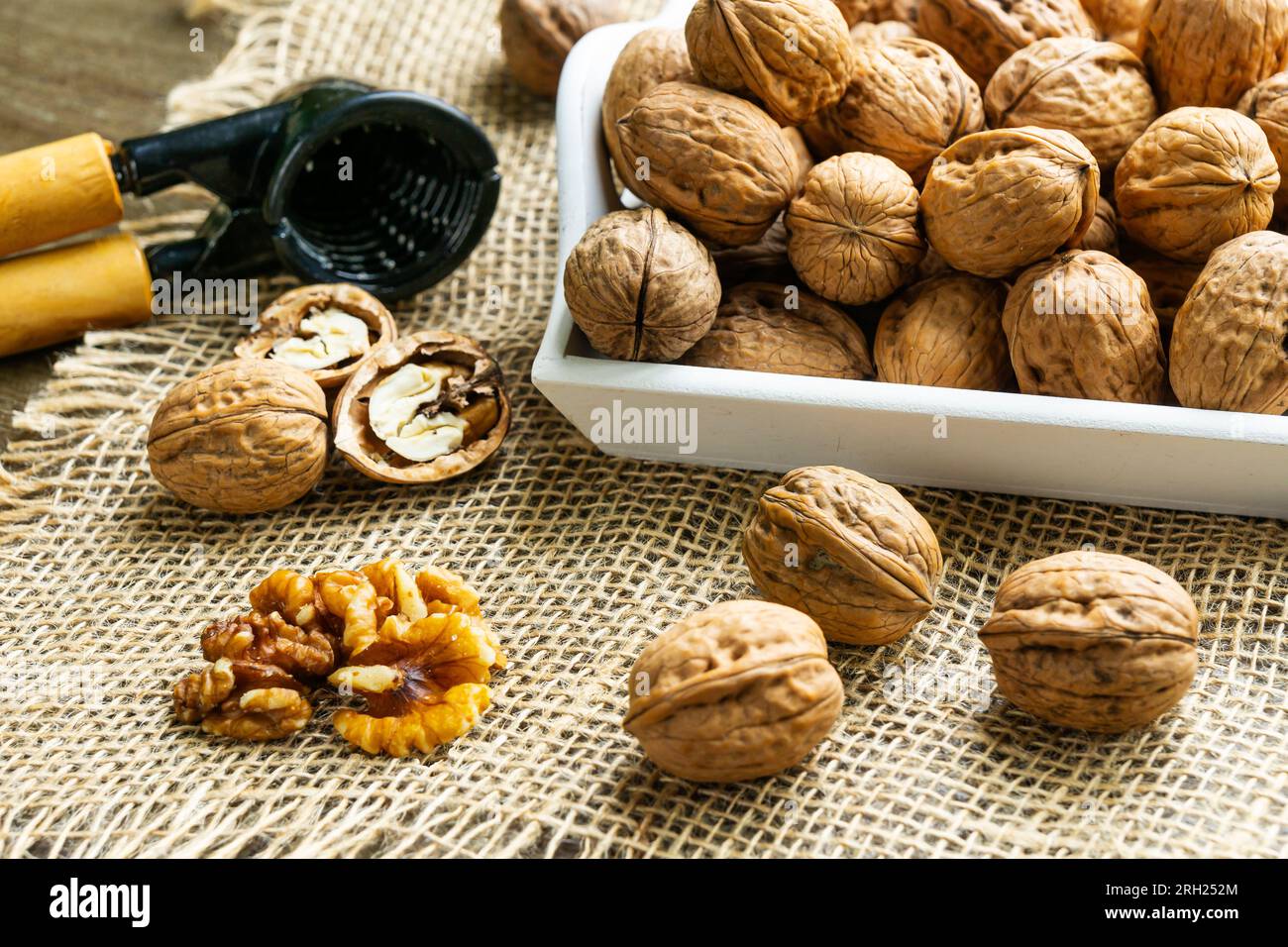 Noci su un vassoio bianco, noci incrinate su un tessuto di rapa e uno schiaccianoci. Foto Stock