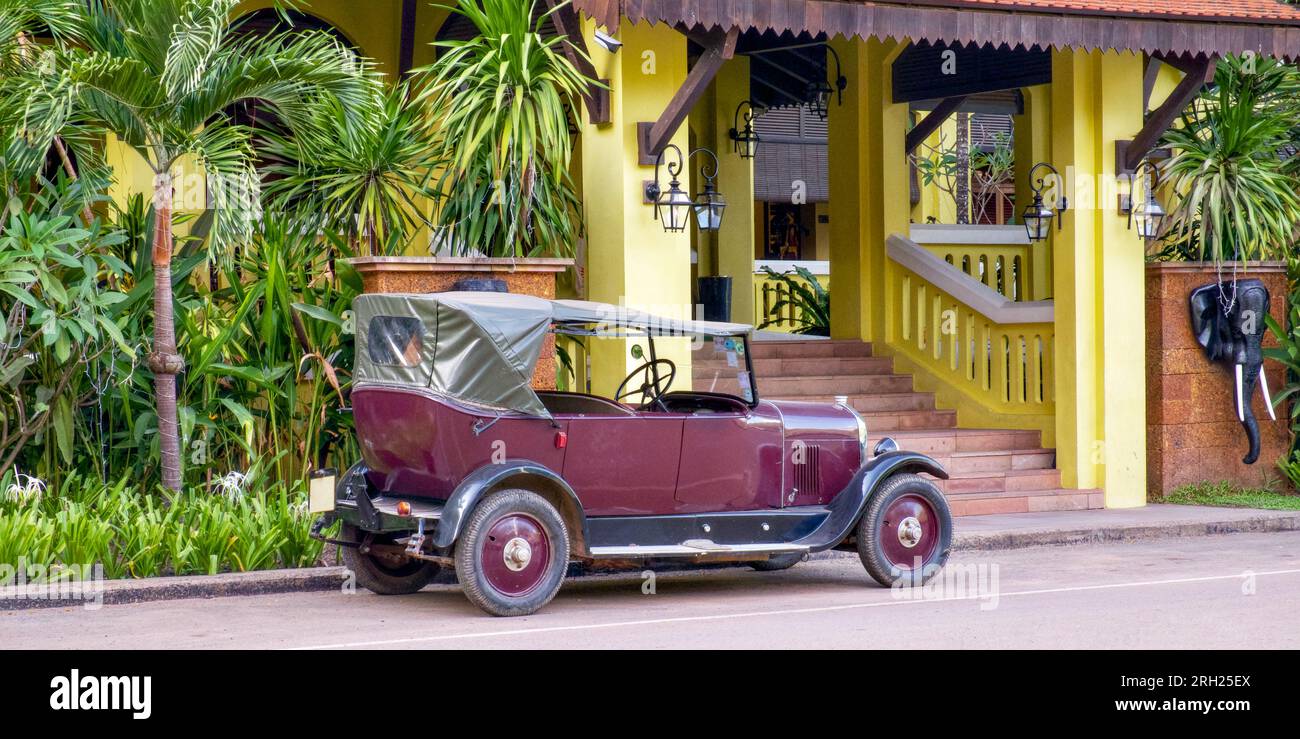 Una bellissima auto retrò con tetto in tela si trova vicino a un edificio giallo in un paese tropicale. Foto Stock