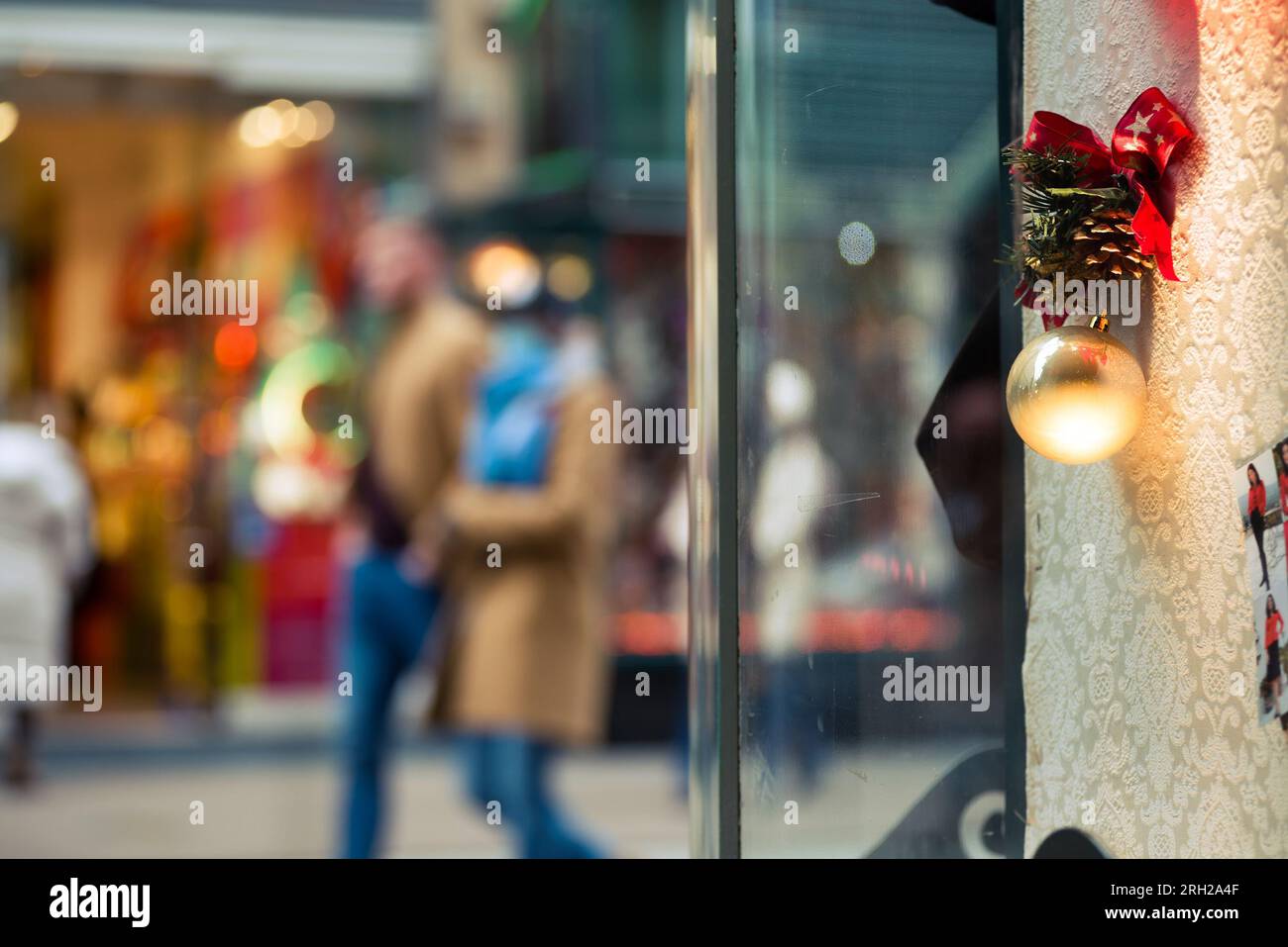 Decorazione con cono di abete e pallone di Natale nella vetrina di un negozio contro persone sfocate. Foto Stock