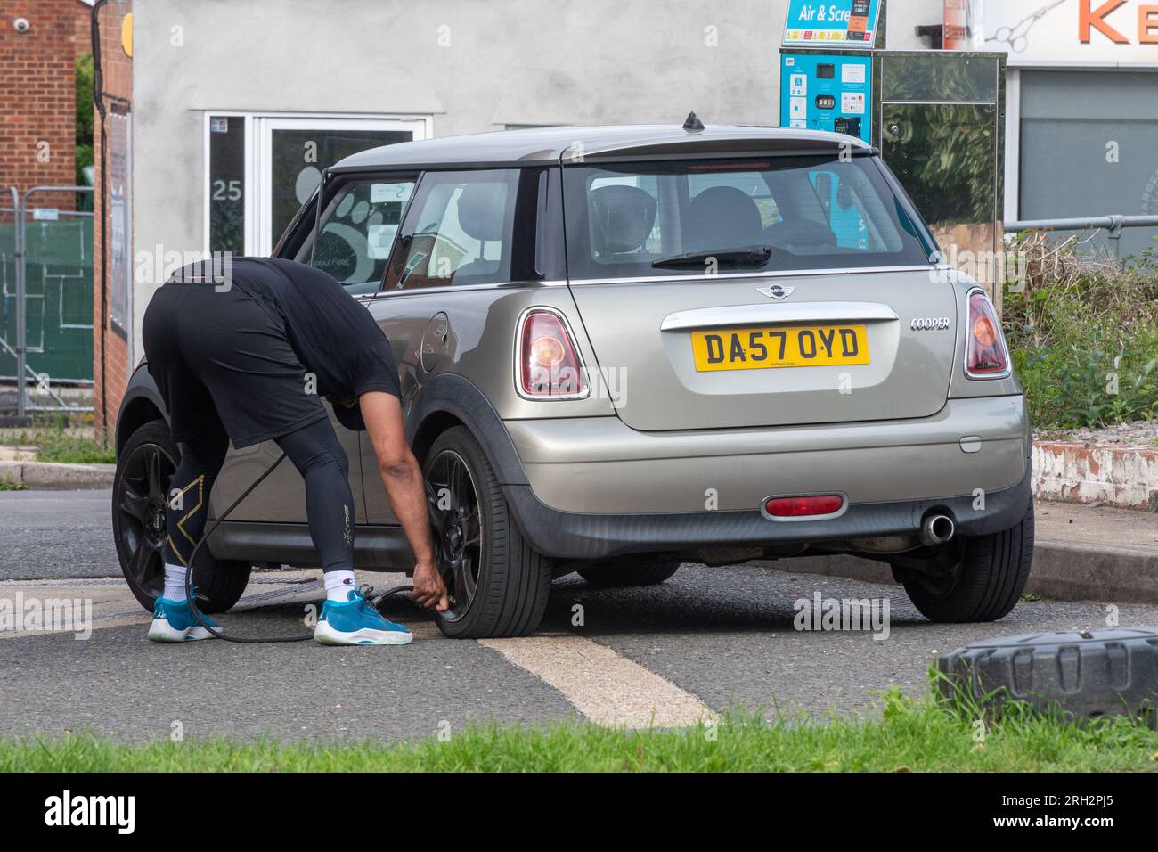 Uomo presso il distributore di benzina di garage che gonfia gli pneumatici su una mini auto utilizzando una pompa di gonfiaggio pneumatici, Inghilterra, Regno Unito Foto Stock
