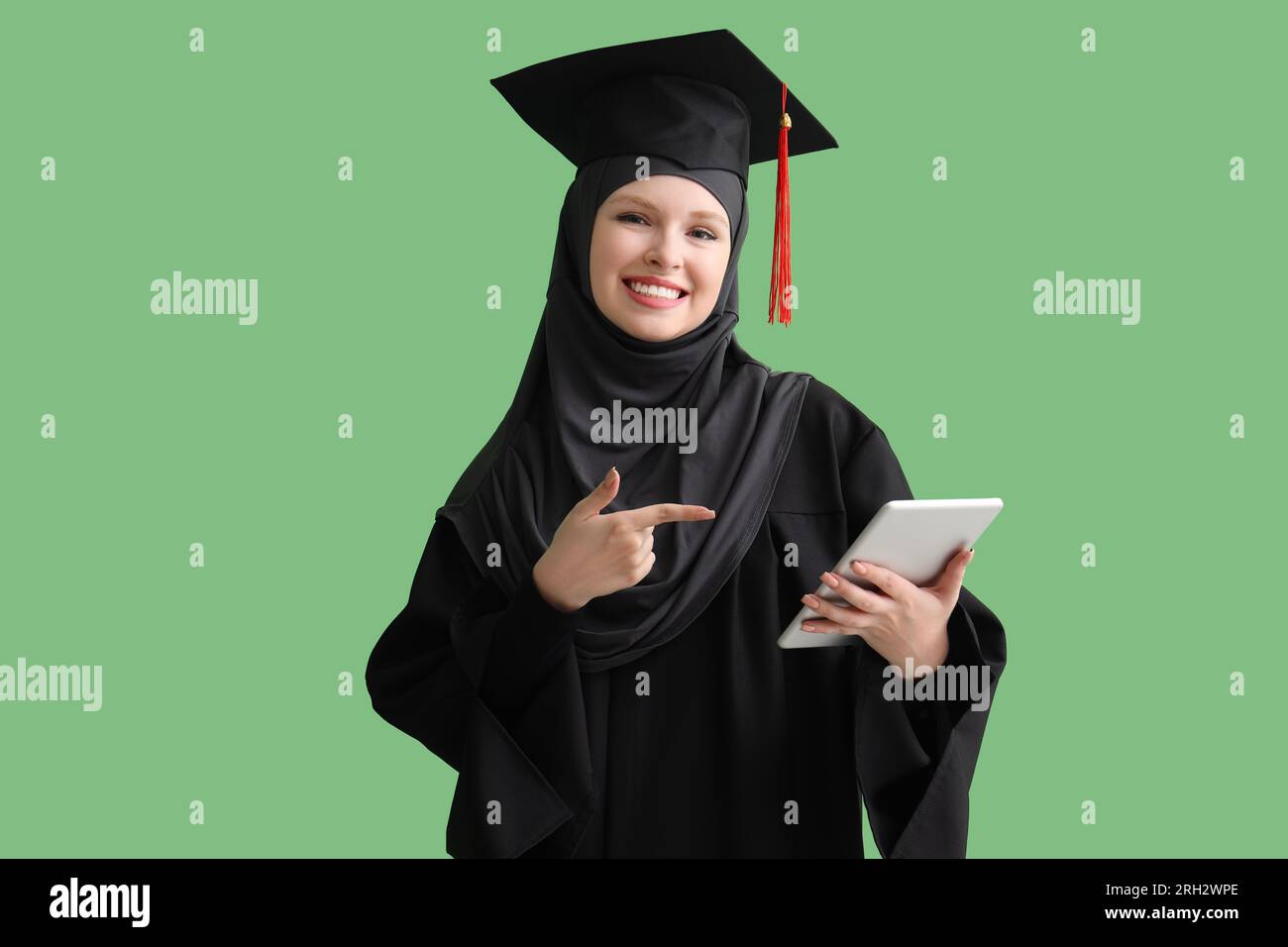 Studente laureato musulmano che punta al computer tablet su sfondo verde Foto Stock