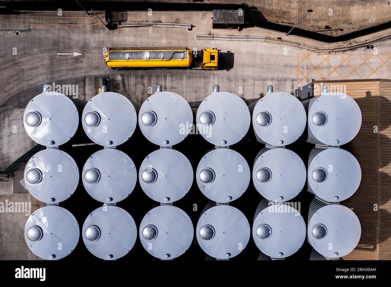 Vista aerea direttamente sopra grandi serbatoi di stoccaggio in fila per la produzione alimentare o lo stoccaggio di sostanze chimiche in un impianto industriale con autocisterna truc Foto Stock