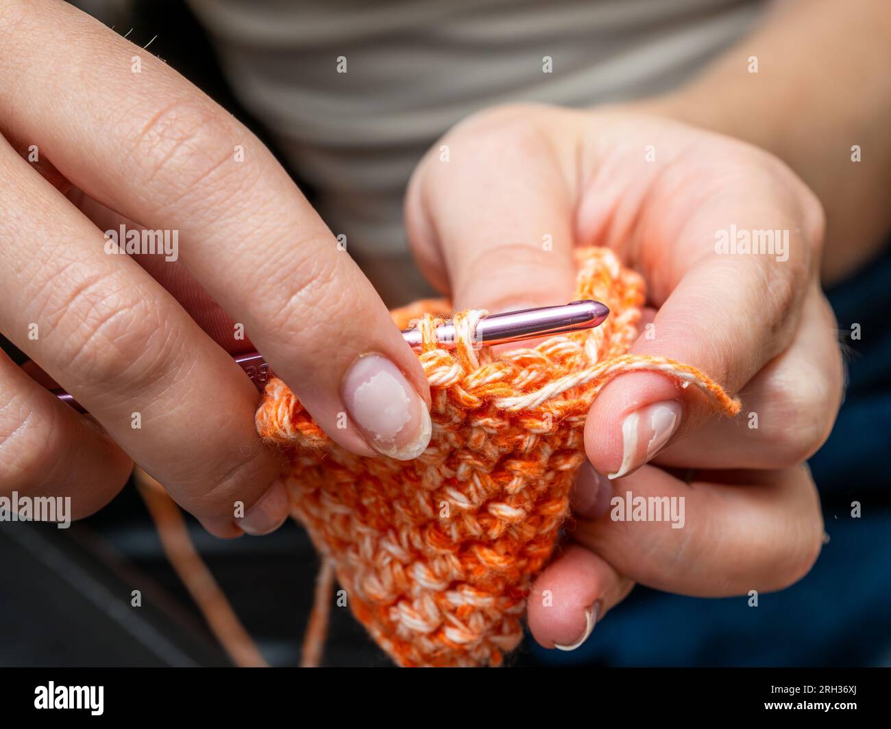 Mani che tengono un uncinetto lavorando su un pezzo d'arte di colore zucca (arancione) Foto Stock