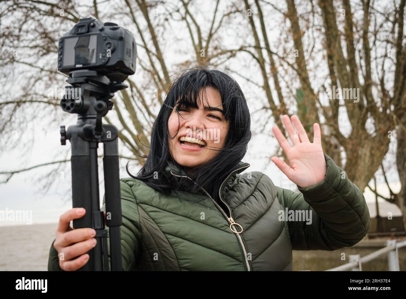 la giovane donna latina venezuelana video blogging con la sua fotocamera digitale che la tiene con la mano e il treppiede, in piedi all'aperto, facendo salti video e sm Foto Stock