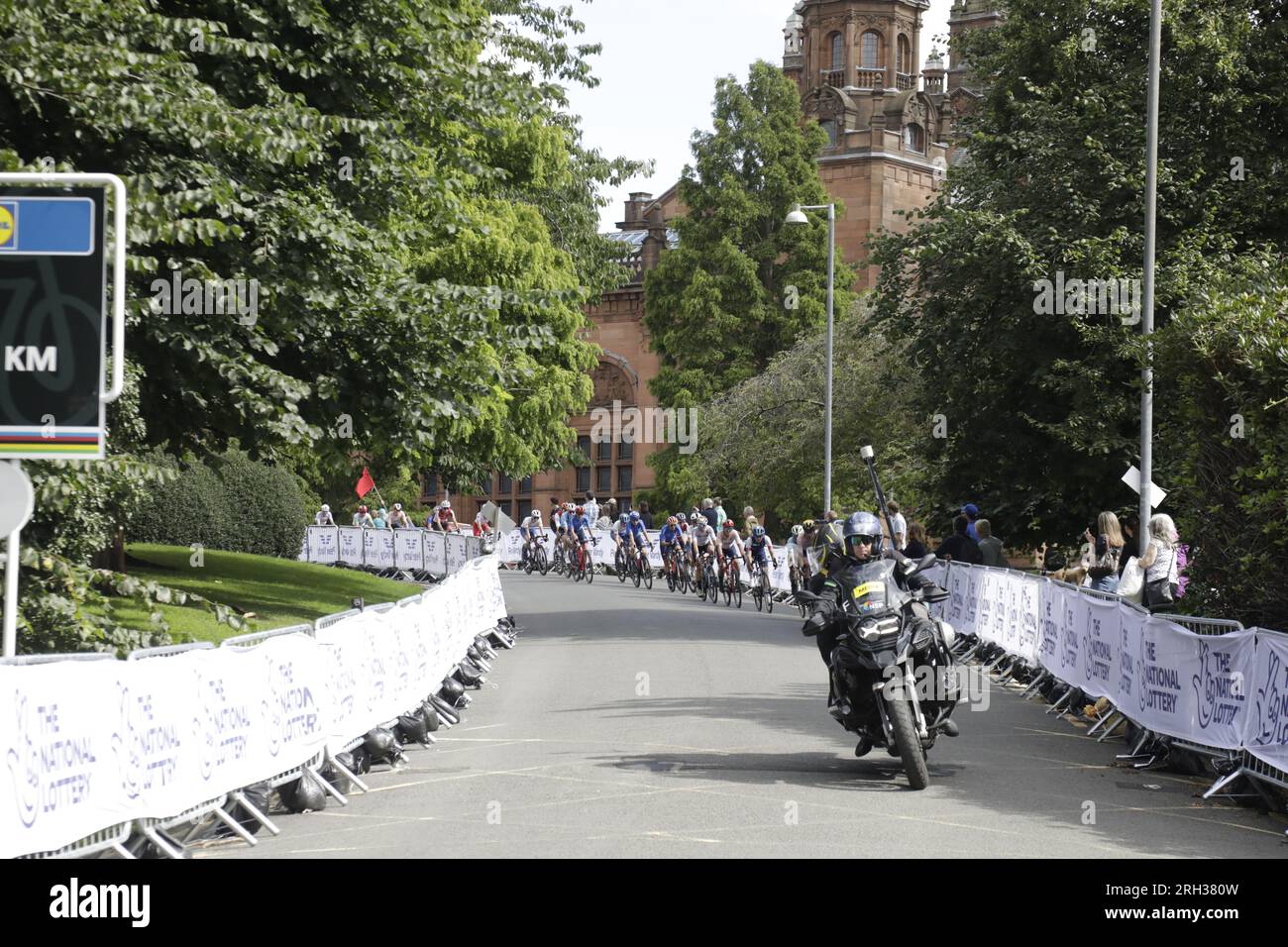 Videografa ufficiale che filma il peloton mentre attraversa Kelvingrove Park durante un giro della città di Glasgow come parte dell'UCI Cycling World Championships Women Elite Road Race. I sostenitori stanno facendo il tifo da dietro le barriere di sicurezza.Glasgow, Scozia, Regno Unito. 13 agosto 2023. Crediti: Elizabeth Leyden/Alamy Live News Foto Stock