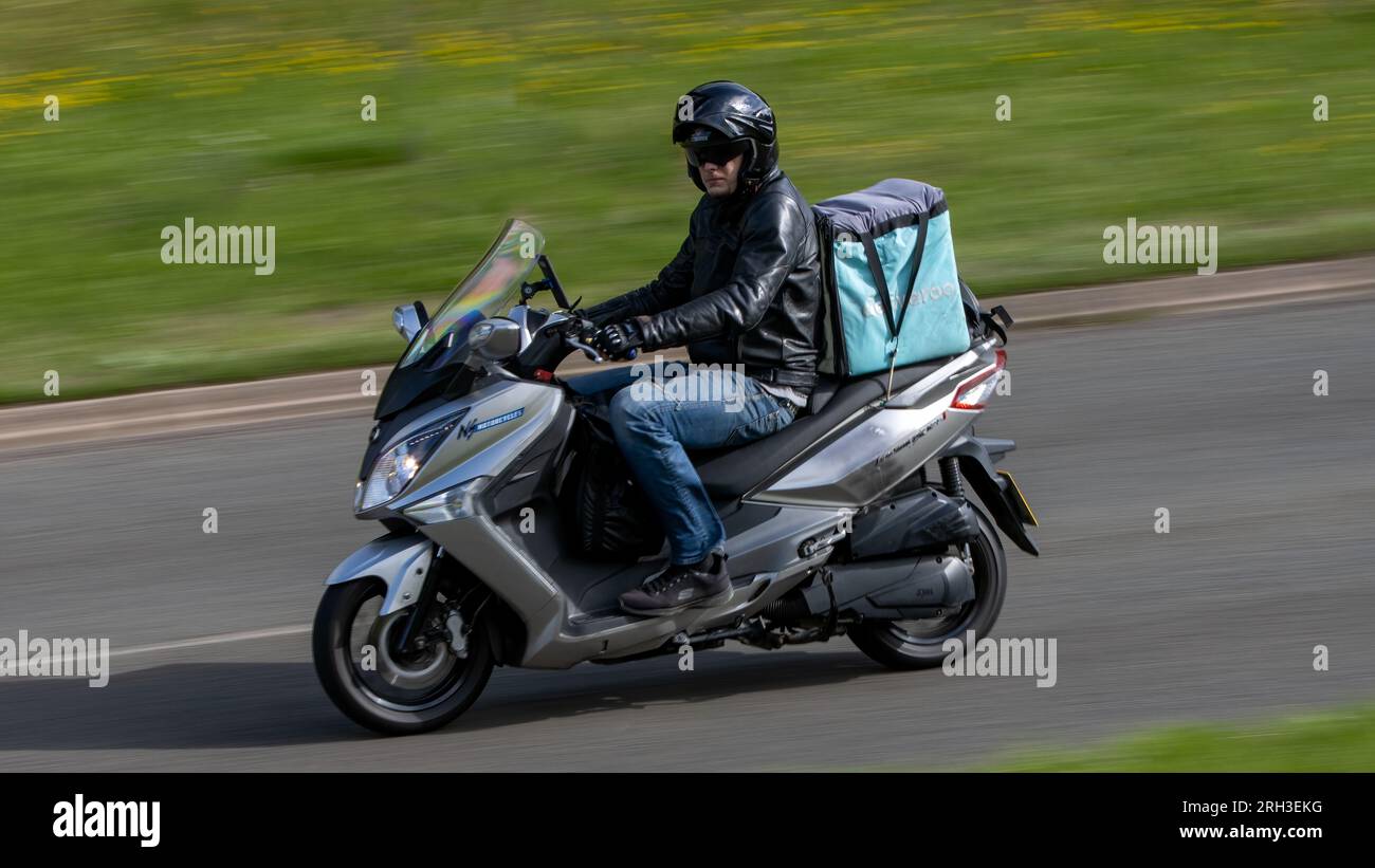Milton Keynes, Regno Unito - 10 agosto 2023: Deliveroo pilota in sella a una moto Sym Joymax su una strada di campagna inglese. Foto Stock