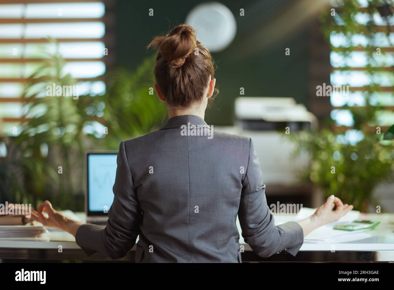 Ambiente di lavoro sostenibile. Vista da dietro la moderna proprietaria di una piccola impresa in un abito da lavoro grigio che meditava. Foto Stock