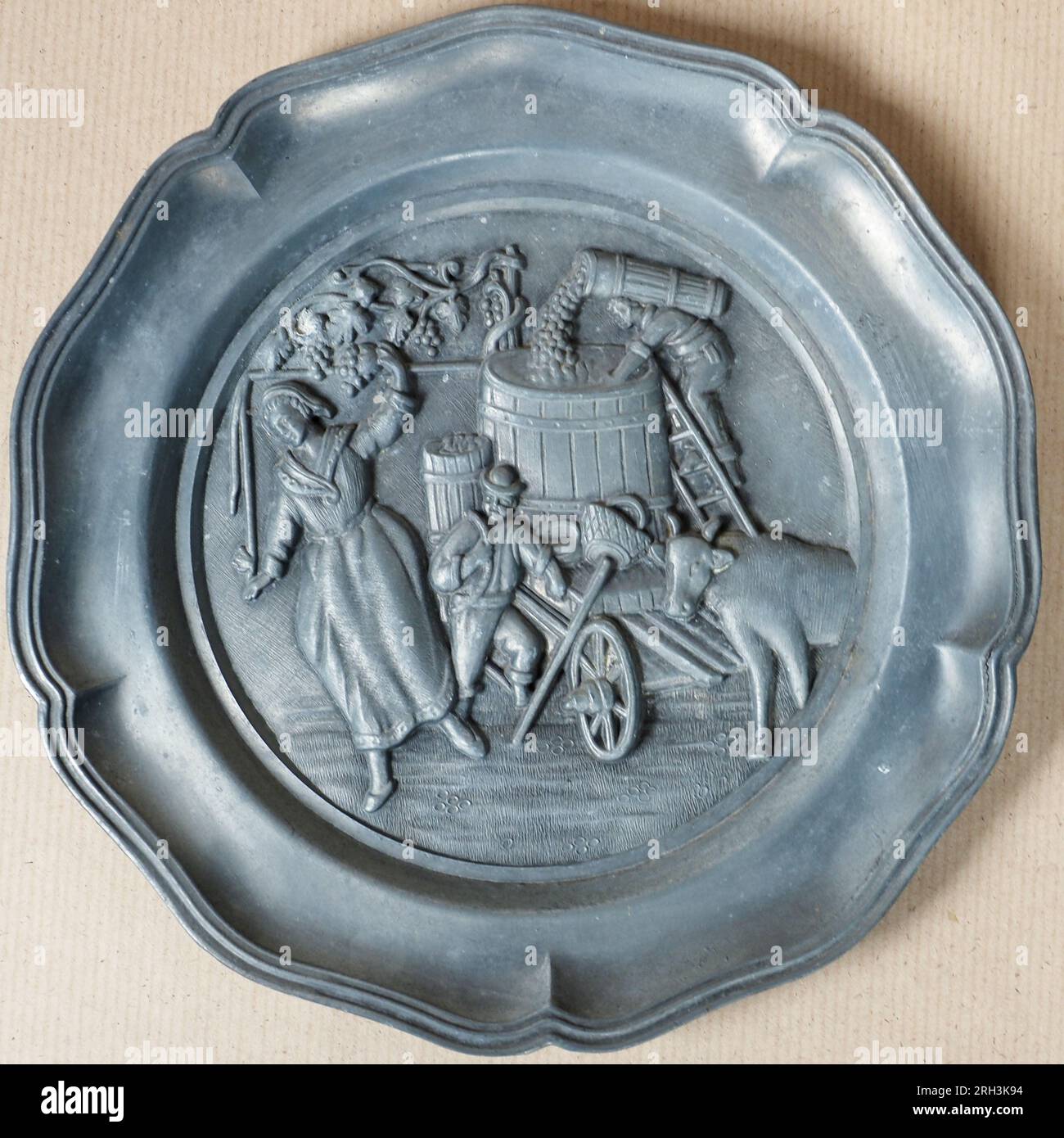 Tradizionale piatto decorativo in peltro antico tedesco che raffigura la scena della produzione di vino d'uva Foto Stock