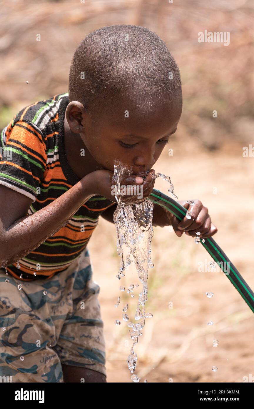 Un giovane ragazzo keniota beve acqua fresca da una pipa con acqua proveniente dal vicino foro, contea di Baringo, Kenya Foto Stock