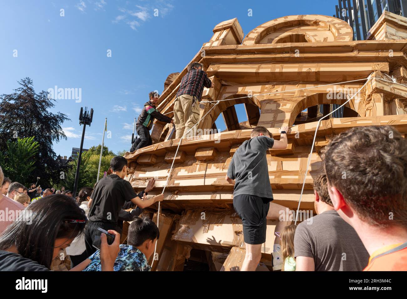 Newcastle upon Tyne, Regno Unito. 13 agosto 2023. Novum Summer Festival - demolizione della "costruzione monumentale" - un edificio in cartone di 45 piedi (14 metri) creato dall'artista visuale francese Olivier Grossetête e da volontari, e poi decostruito. Novum è un nuovissimo festival multi-arte che mette in mostra talenti locali, nazionali e internazionali presso il Centro Civico della città. -- l'edificio è distrutto dal pubblico. Crediti: Hazel Plater/Alamy Live News Foto Stock