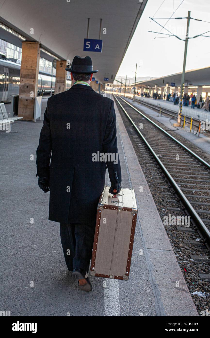 Uomo che cammina con la valigia alla stazione ferroviaria. Uomo che cammina lungo la piattaforma con valigia pesante. Foto Stock