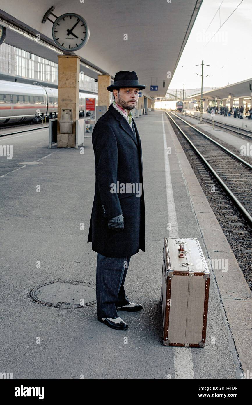 Viaggiatore di sesso maschile in attesa di viaggiare sulla piattaforma ferroviaria. Uomo in piedi con bagagli alla stazione centrale, treno in orario o in ritardo. Foto Stock