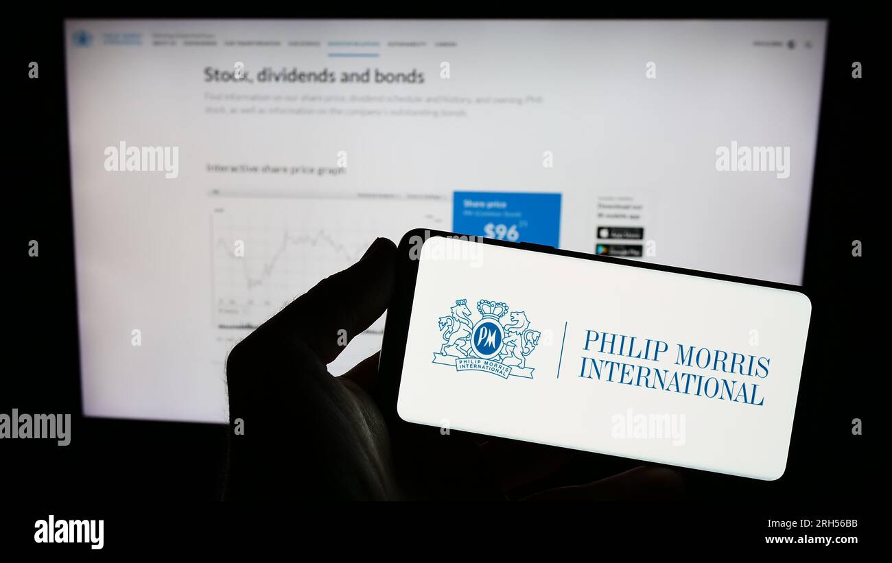 Persona che possiede un telefono cellulare con il logo dell'azienda americana Philip Morris International Inc. Sullo schermo davanti alla pagina Web. Concentrarsi sul display del telefono. Foto Stock