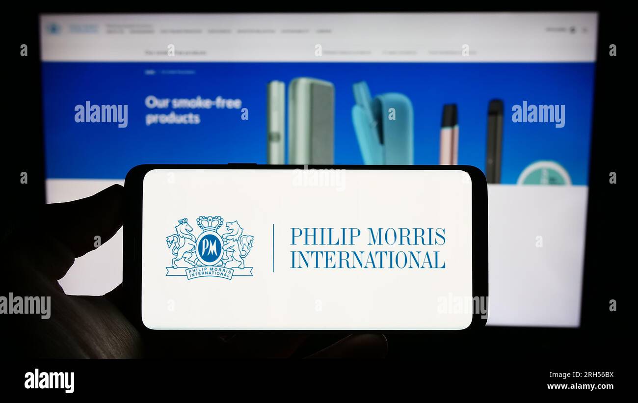 Persona che possiede il cellulare con il logo della società statunitense Philip Morris International Inc. Sullo schermo davanti alla pagina Web aziendale. Concentrarsi sul display del telefono. Foto Stock