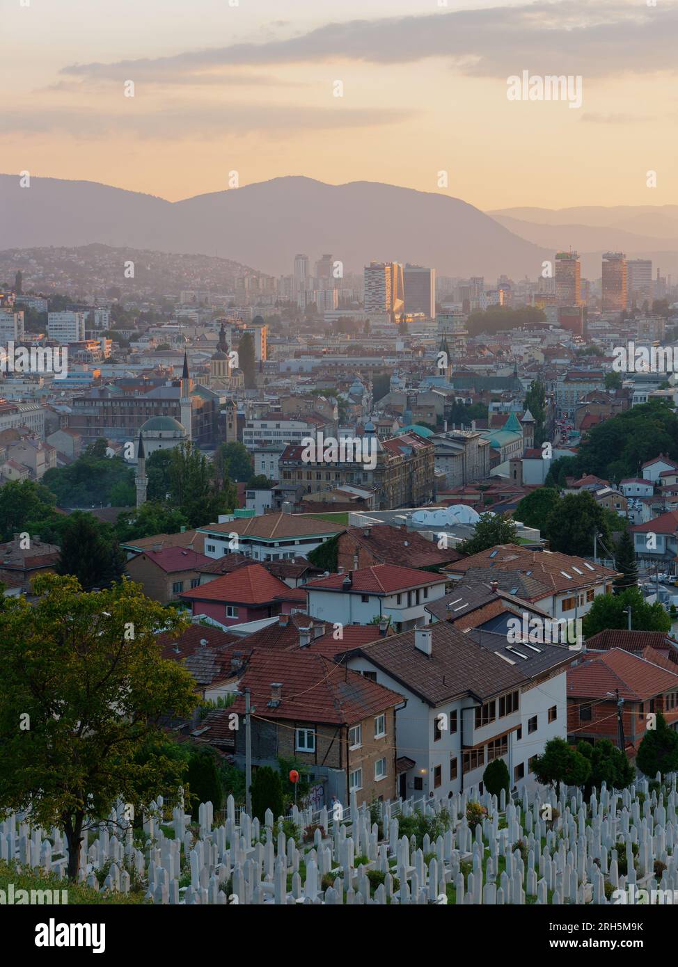 Vista su Sarajevo al tramonto con blocchi di appartamenti e montagne sullo sfondo, cimitero in primo piano, Bosnia ed Erzegovina, 13 agosto 2023. Foto Stock