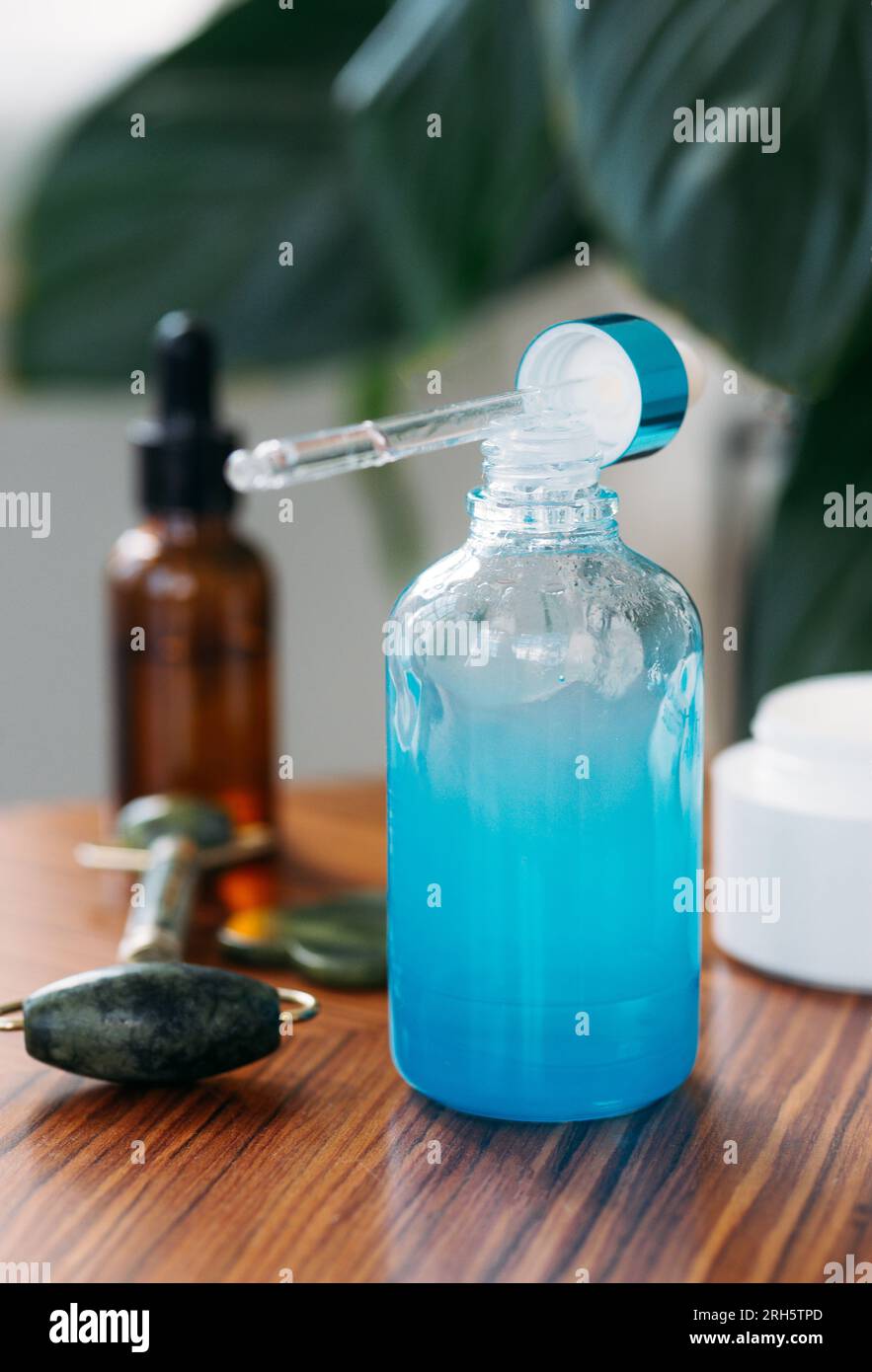 Olio aromatico essenziale o essenza di siero in bottiglia di vetro blu su un tavolo di legno su uno sfondo di piante verdi e prodotti di bellezza. Concetto di cos Foto Stock