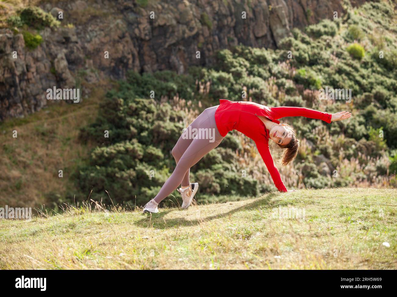 Una giovane donna che indossa leggings che si allunga in un parco pubblico di Edimburgo Foto Stock