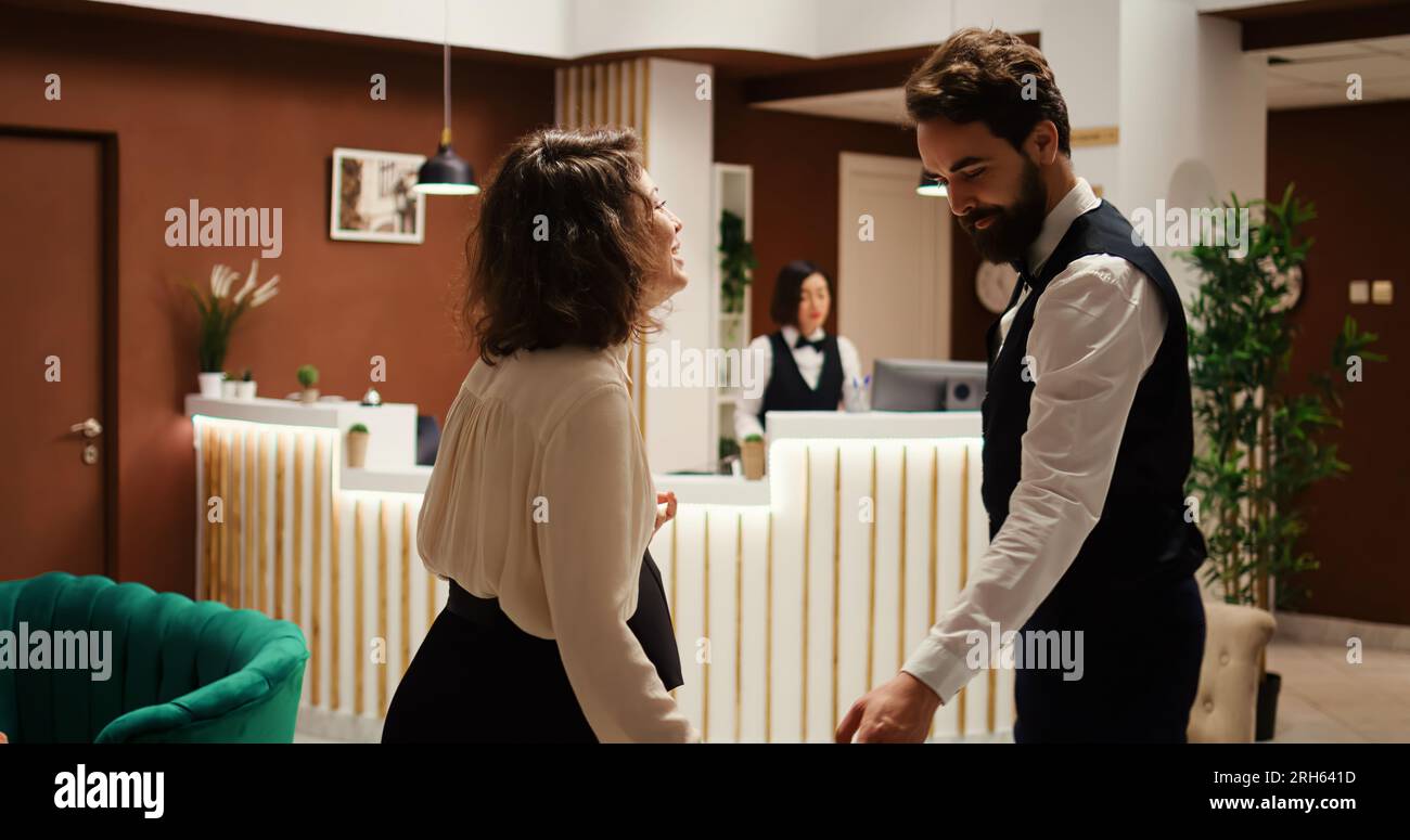 Donna d'affari che effettua il check-in in un hotel di lusso, aiutata dal fattorino con i bagagli mentre la receptionist controlla i dettagli della prenotazione. Visitatore del residence in viaggio professionale assistito dal personale di portineria Foto Stock