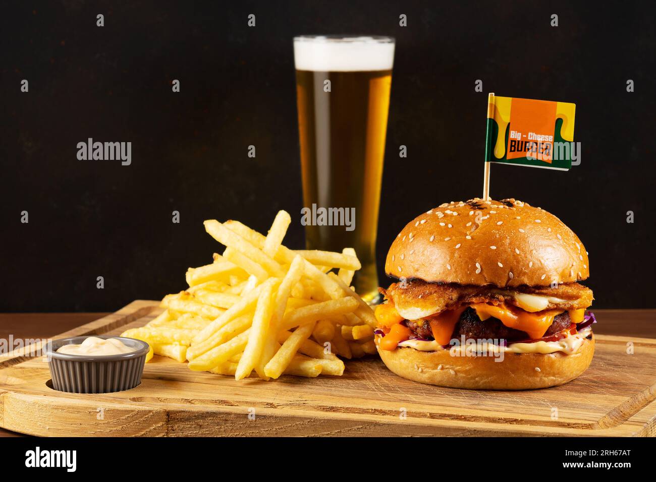 Concetto di fast food. Gustoso cheeseburger con patate fritte in padella e un bicchiere di birra su un tavolo di legno. Foto Stock