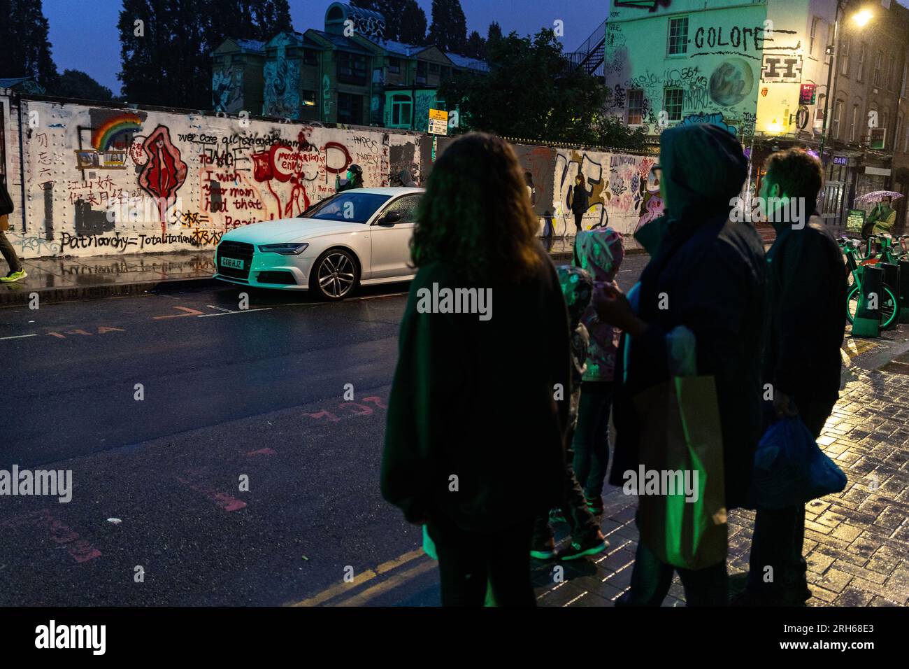 Londra, Regno Unito. 8 agosto 2023. Gli spettatori guardano gli slogan anti-Pechino a Brick Lane. "Brick Lane a East London, storicamente celebrata per la sua eclettica Street art, è stata recentemente coinvolta in una controversa guerra dei graffiti. Il conflitto è iniziato sabato 5, quando un gruppo di artisti ha mostrato i "12 valori socialisti fondamentali" del Partito Comunista Cinese. In 24 caratteri cinesi rossi in grassetto su una parete di 100 metri. Questi valori sono "prosperità", "democrazia", "civiltà" e "armonia"; i valori sociali di "libertà", "uguaglianza", "giustizia" e "Stato di diritto"; e in Foto Stock